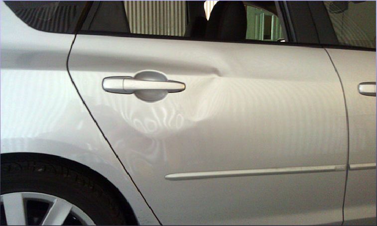 A dent and crease in the silver door panel of a car before paintless repair