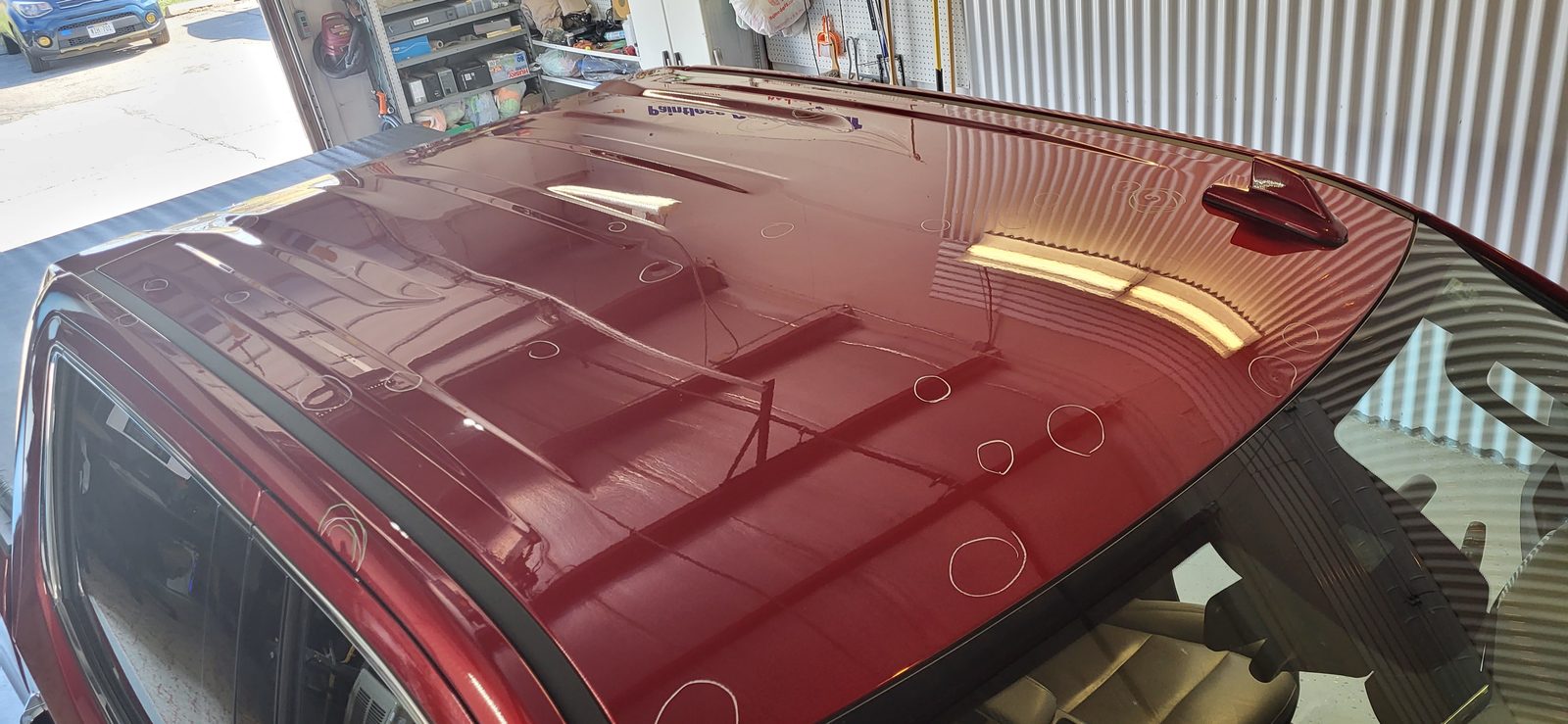 Dozens of hail dents across the dark red roof of a car before repair